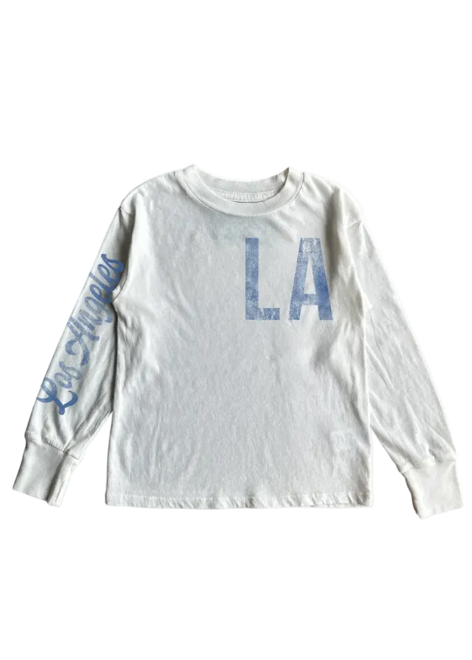 A white long-sleeve t-shirt with a distressed blue 'LA' print on the chest and 'Los Angeles' script on the sleeve, shown flat on a white background.