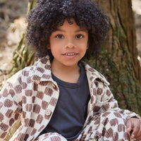 Child sitting outdoors in front of a tree wearing a patterned coat.