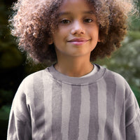 Child wearing a gray sweater with a blurred green background