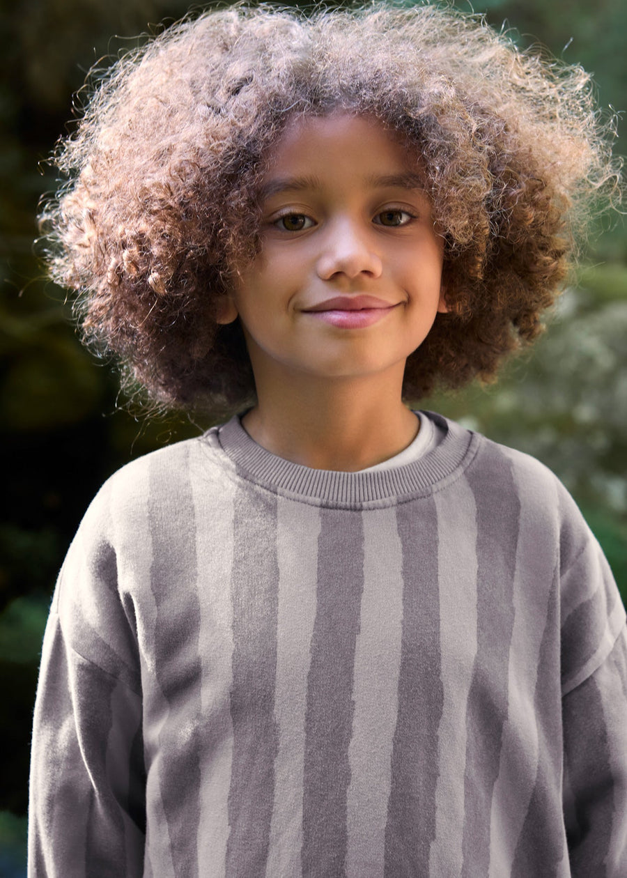Child wearing a gray sweater with a blurred green background