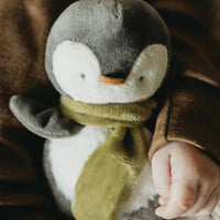Child's hand holding a plush penguin toy with a green scarf against a brown background
