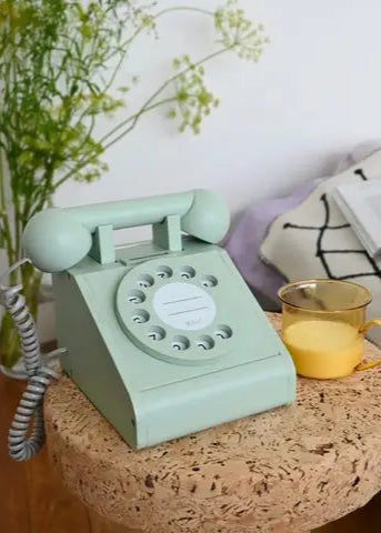 Vintage green telephone on a cork table with a cup of tea and decorative elements.