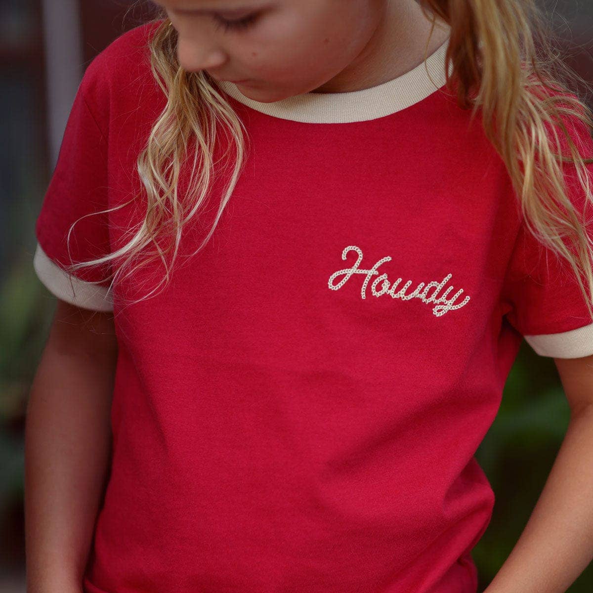Person wearing a red shirt with 'Howdy' embroidered on it, blurred background