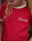 Person wearing a red shirt with 'Howdy' embroidered on it, blurred background