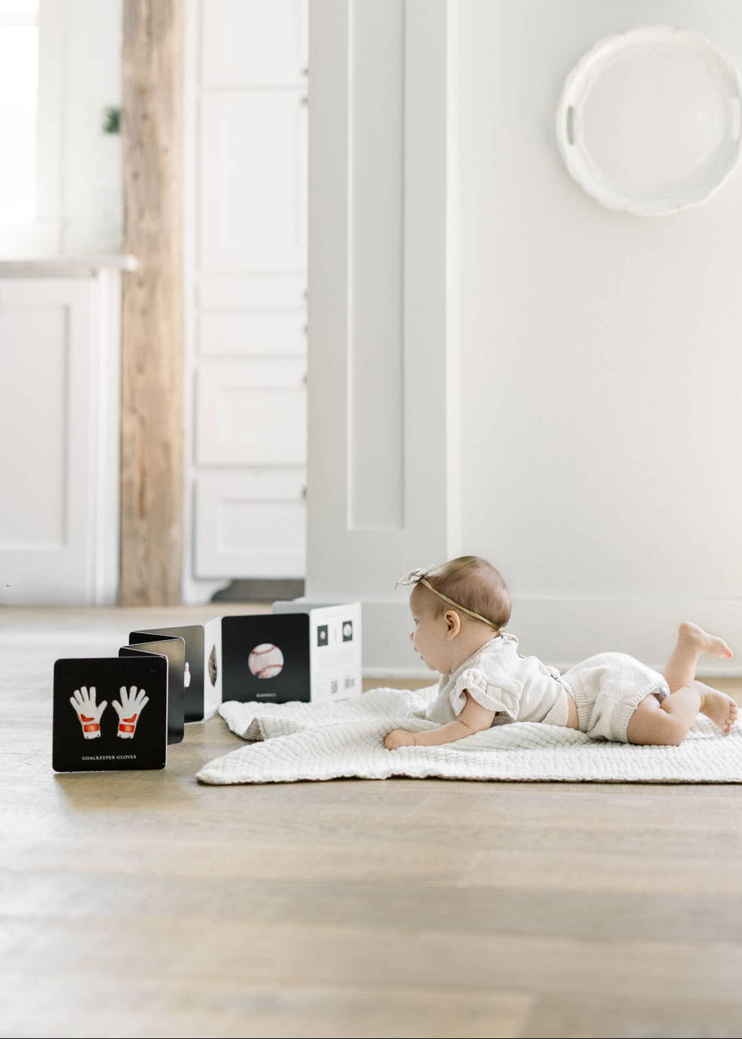 Baby lying on a white rug in a minimalistic room with white walls and wooden floor.