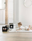 Baby lying on a white rug in a minimalistic room with white walls and wooden floor.