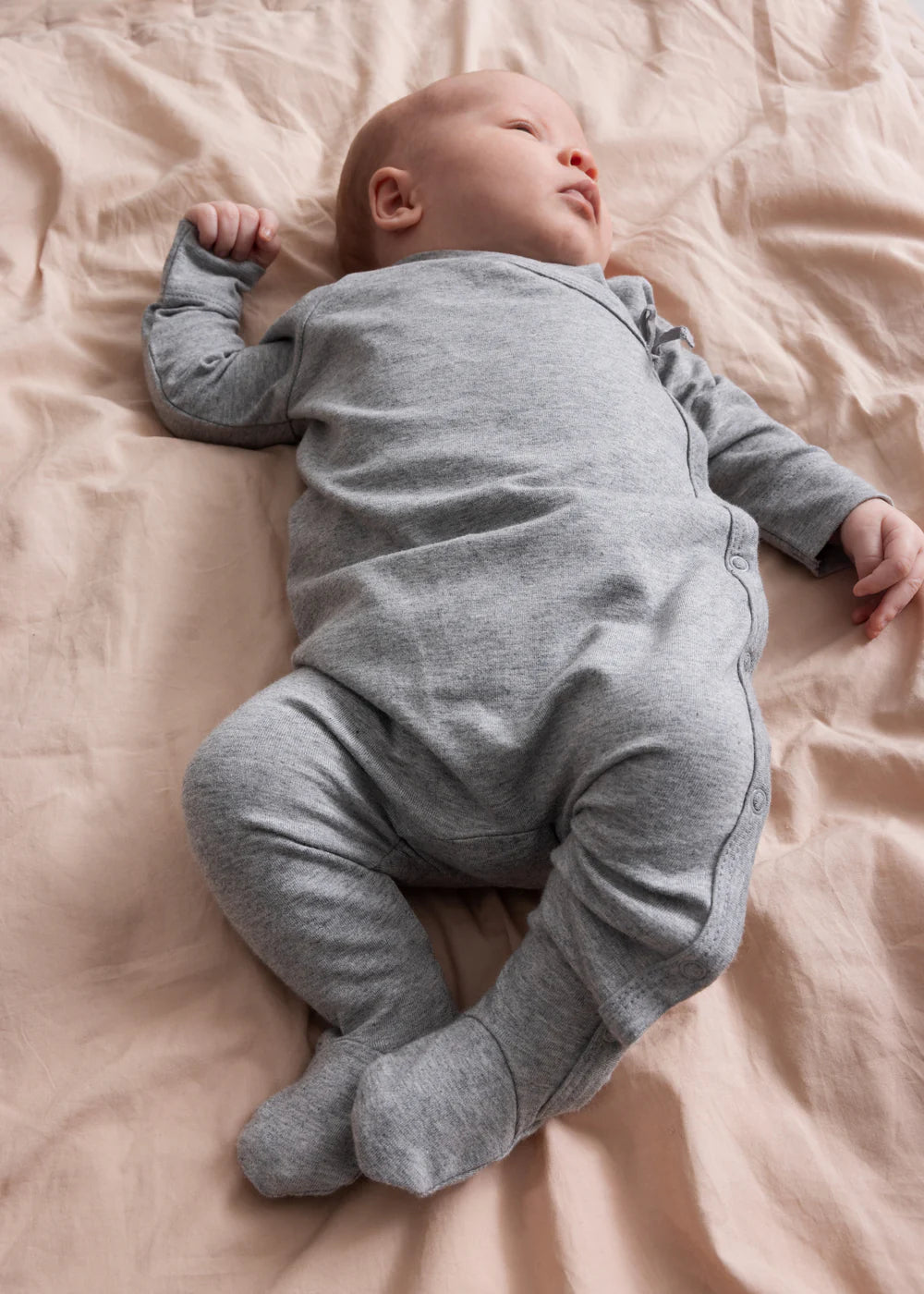 Baby in a gray onesie lying on a pink blanket