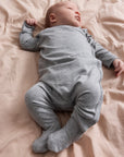 Baby in a gray onesie lying on a pink blanket