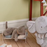 Gray elephant plush toy on a wooden floor with children's toys and a small table in the background.