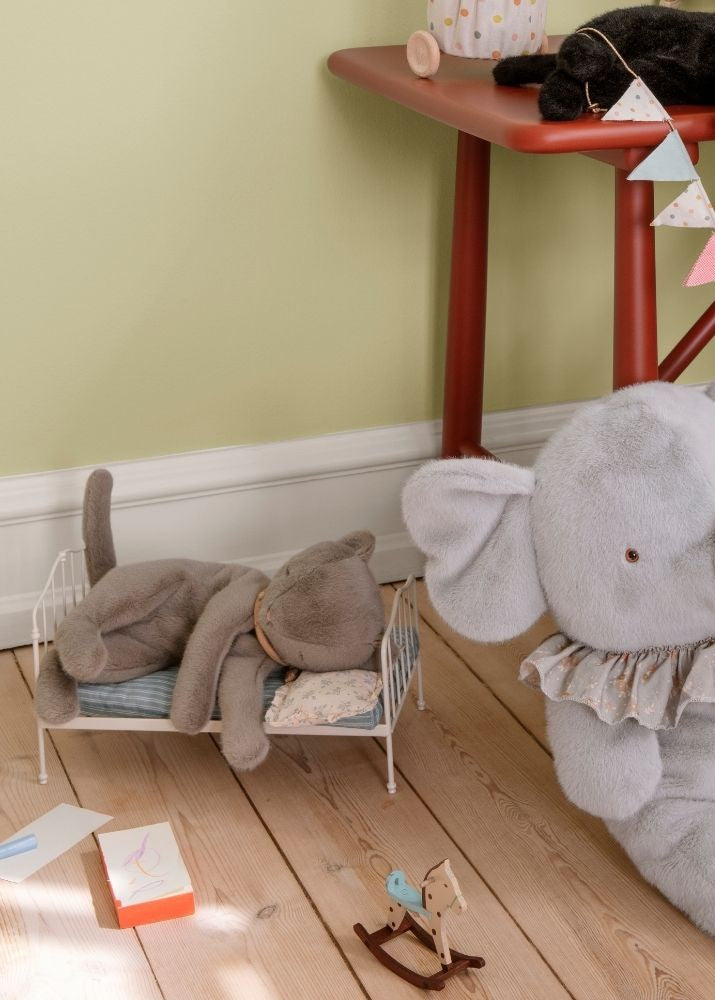 Gray elephant plush toy on a wooden floor with children's toys and a small table in the background.