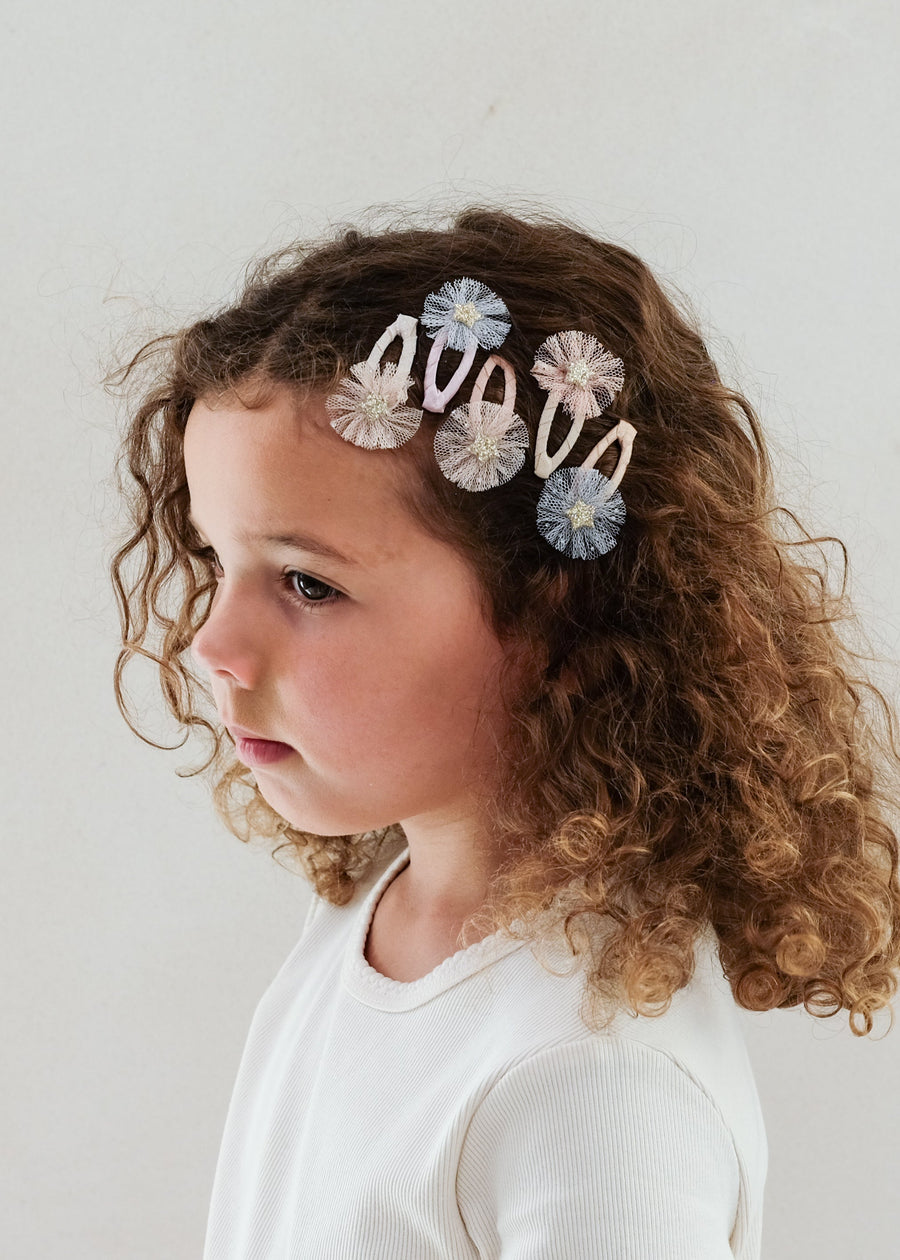 Young girl with curly hair wearing decorative hair clips against a plain background