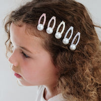 Child with a decorative hair accessory featuring pearls and beads on a plain background