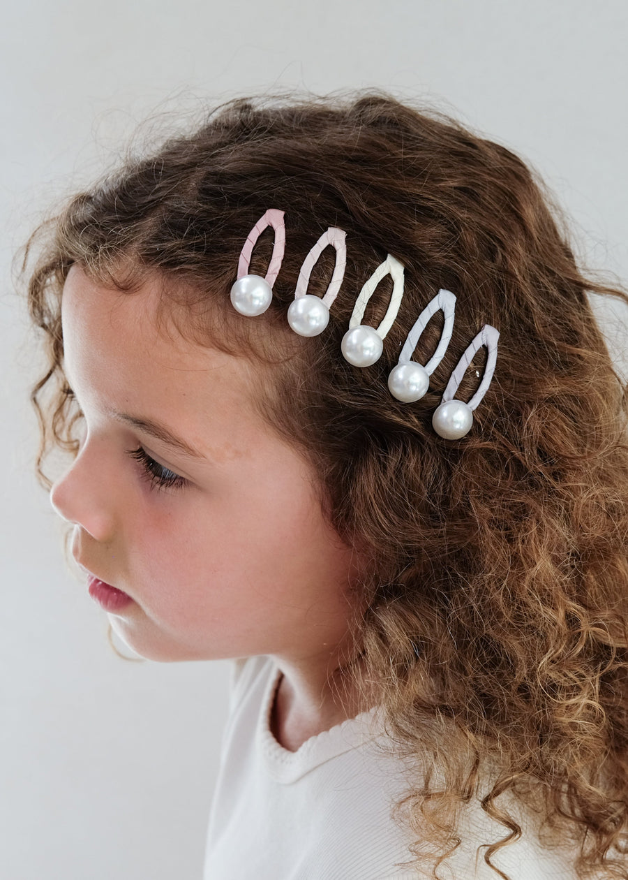 Child with a decorative hair accessory featuring pearls and beads on a plain background