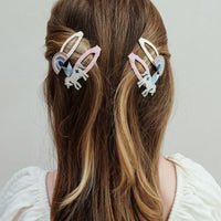 Person with long hair wearing two colorful hair clips on a plain background