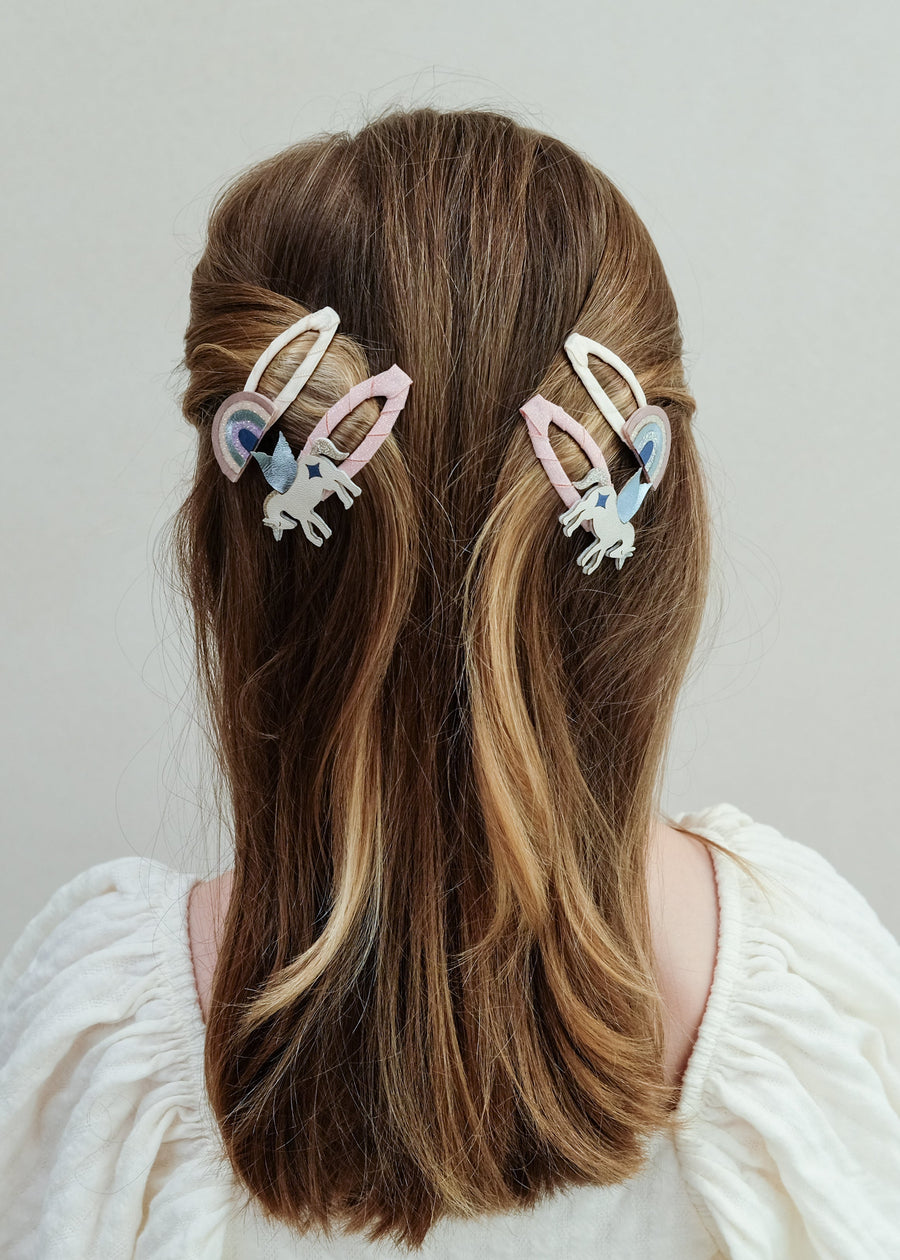Person with long hair wearing two colorful hair clips on a plain background