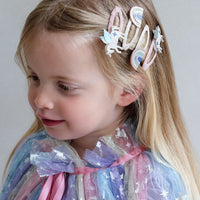 Young girl with decorative hair clips and a colorful cape against a plain background