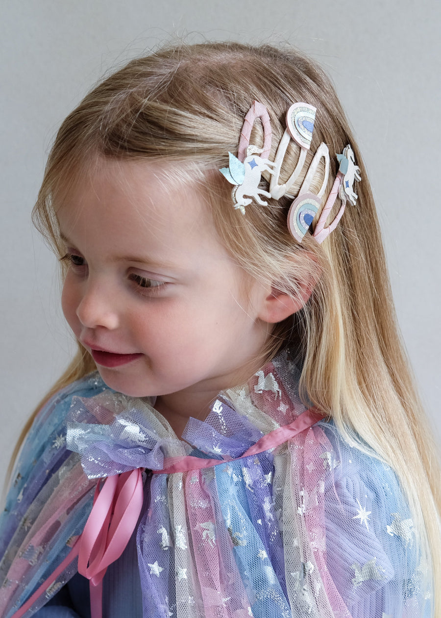 Young girl with decorative hair clips and a colorful cape against a plain background