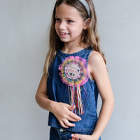 Young girl wearing a denim dress with a colorful flower accessory against a plain background