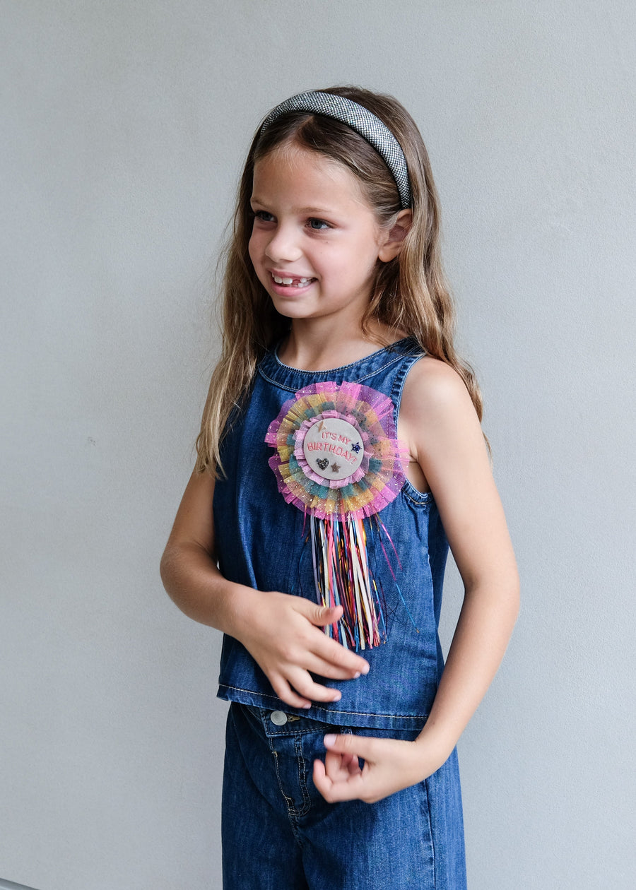 Young girl wearing a denim dress with a colorful flower accessory against a plain background