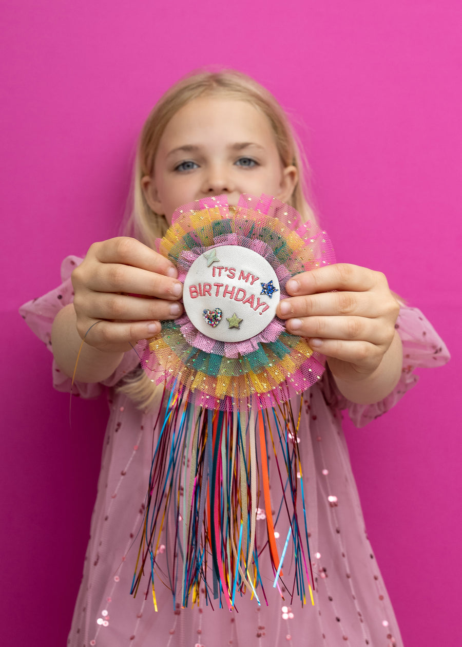 Young girl holding a colorful birthday decoration against a pink background