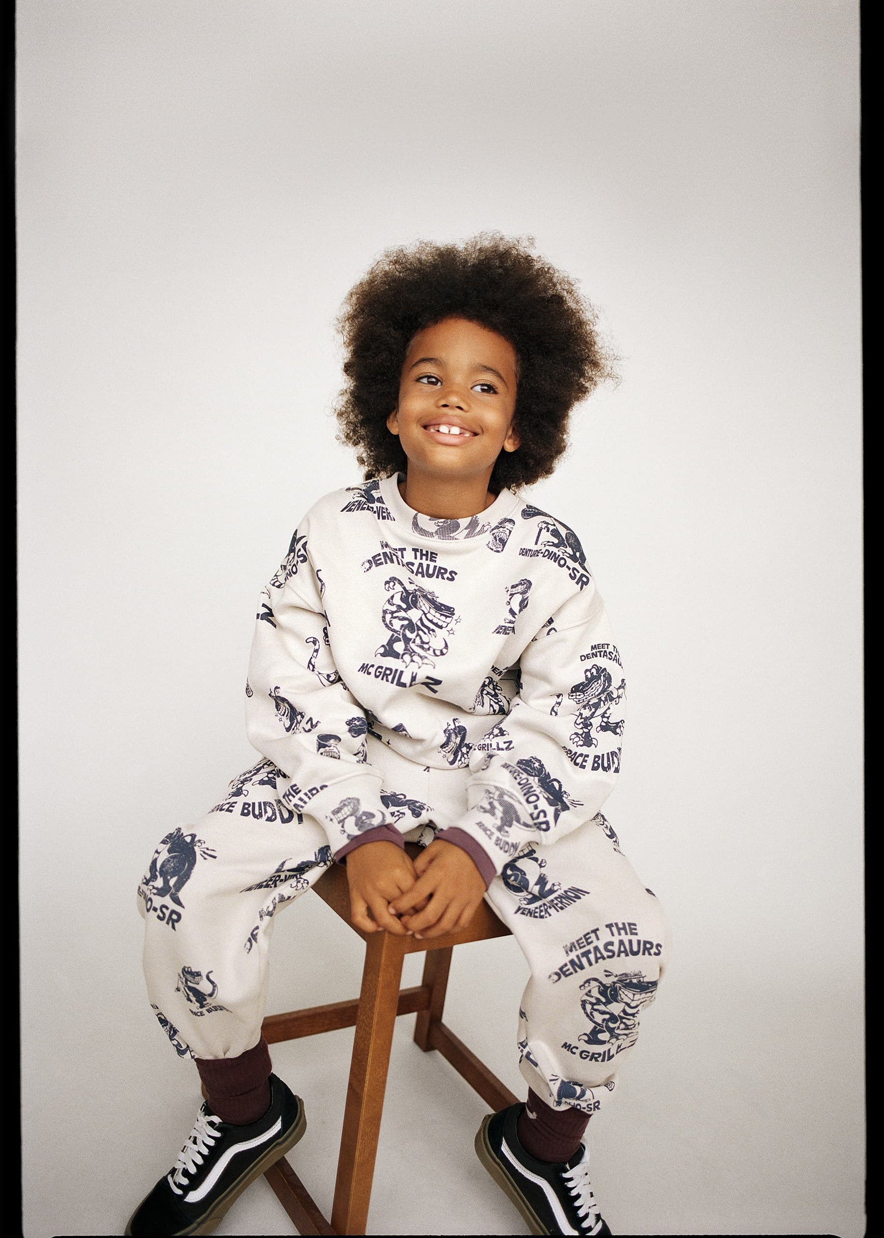 Child wearing a white pajama set with animal prints sitting on a stool against a plain background