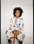 Child wearing a white pajama set with animal prints sitting on a stool against a plain background