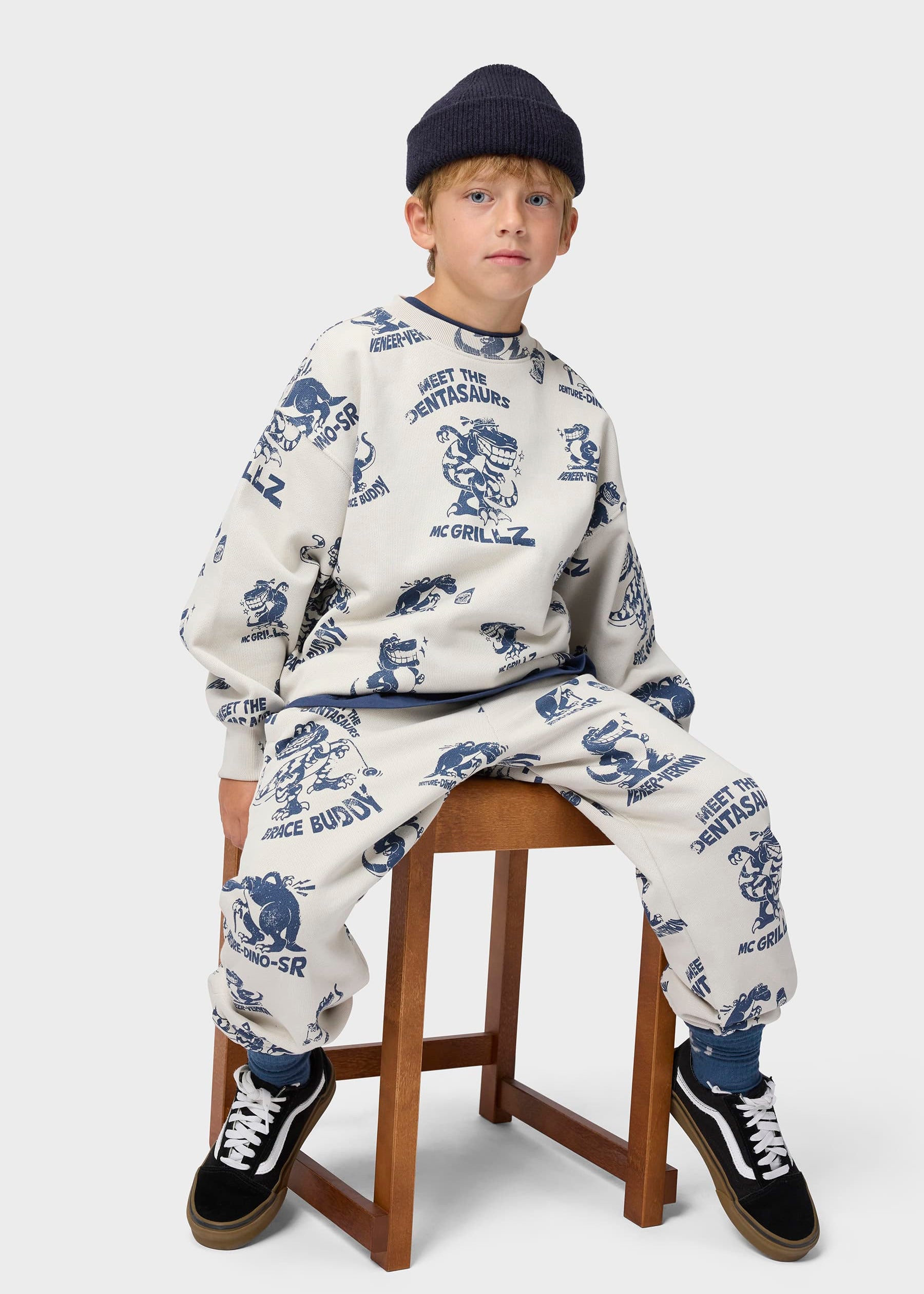 Child wearing a patterned outfit sitting on a stool against a white background
