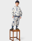 Child wearing a patterned outfit standing on a wooden stool against a white background