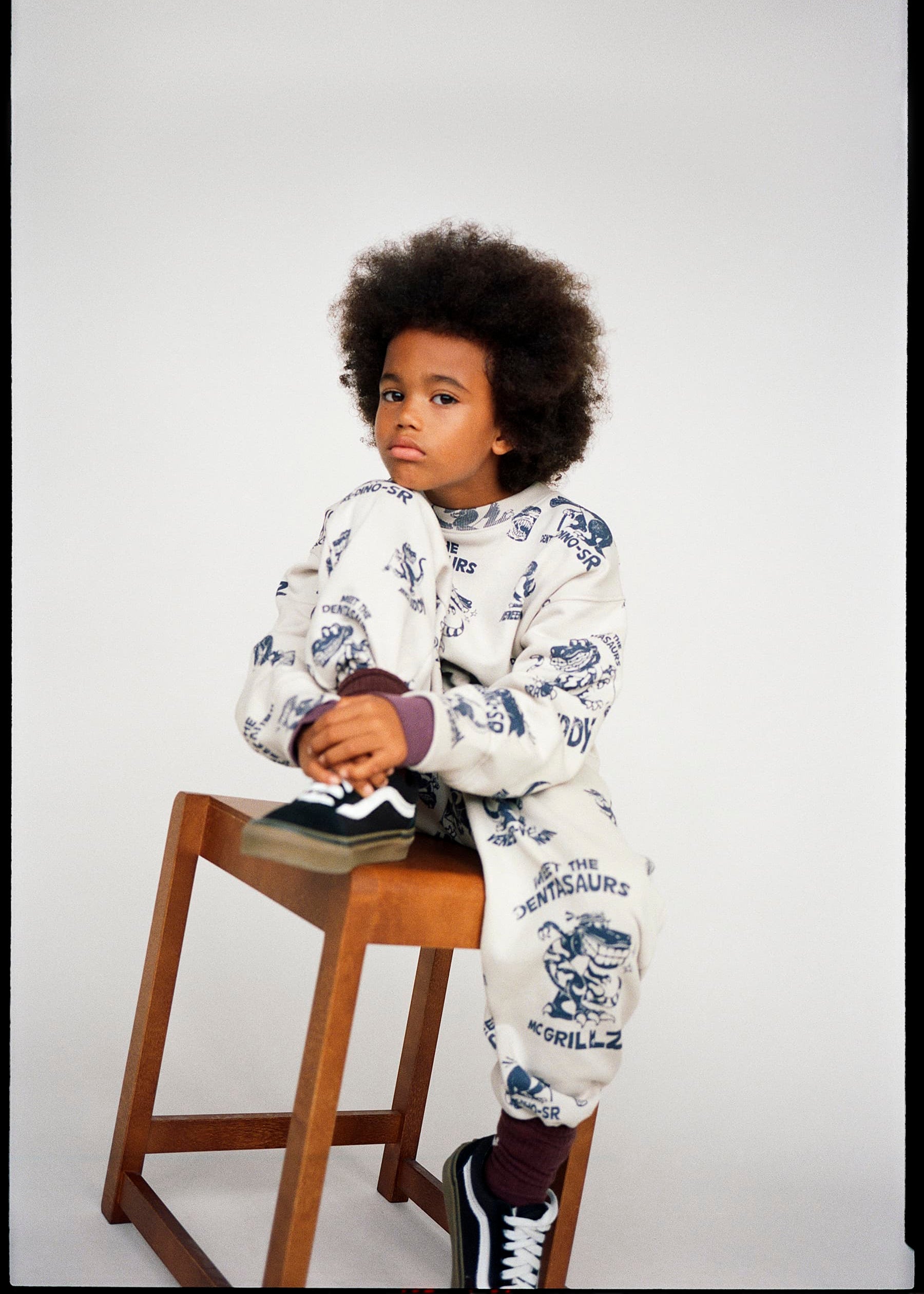 Child sitting on a wooden stool wearing a patterned outfit against a plain background