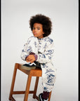 Child sitting on a wooden stool wearing a patterned outfit against a plain background
