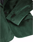 Close-up of a dark green velvet blazer jacket showing the fabric texture, a buttoned cuff with three buttons, and a lapel detail against a white background.