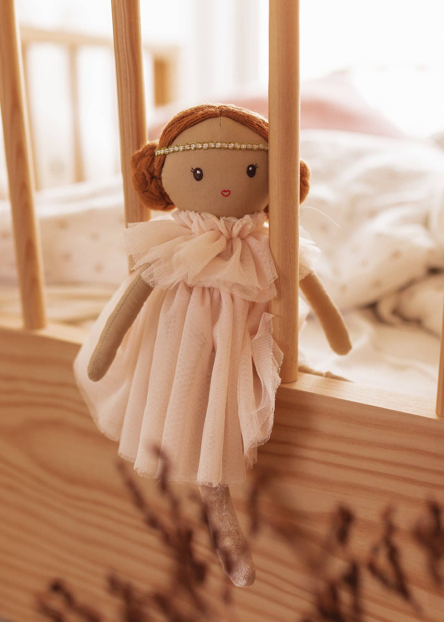 Small doll with a pink dress hanging inside a wooden crib