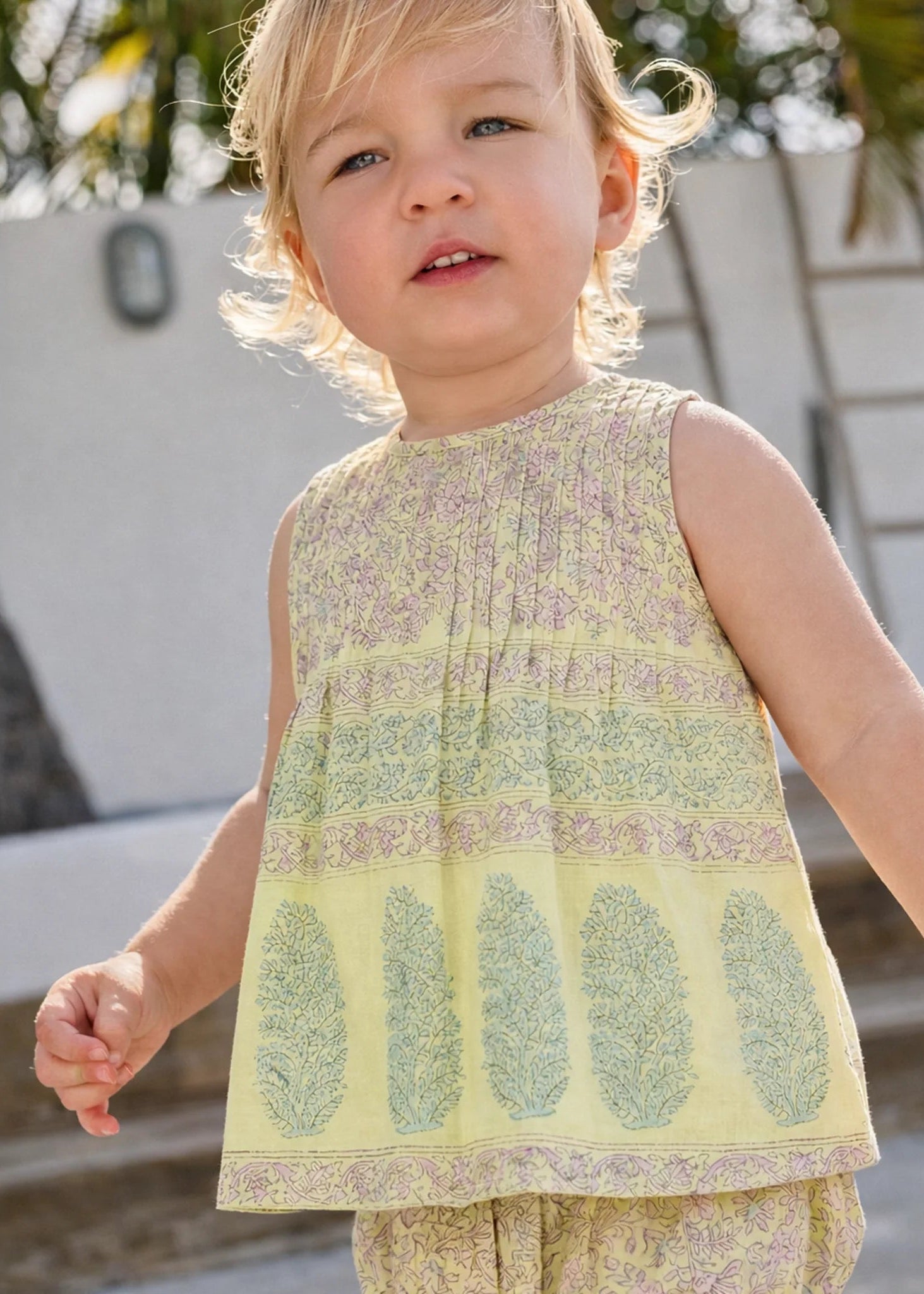 Child wearing a patterned sleeveless top and pants outdoors