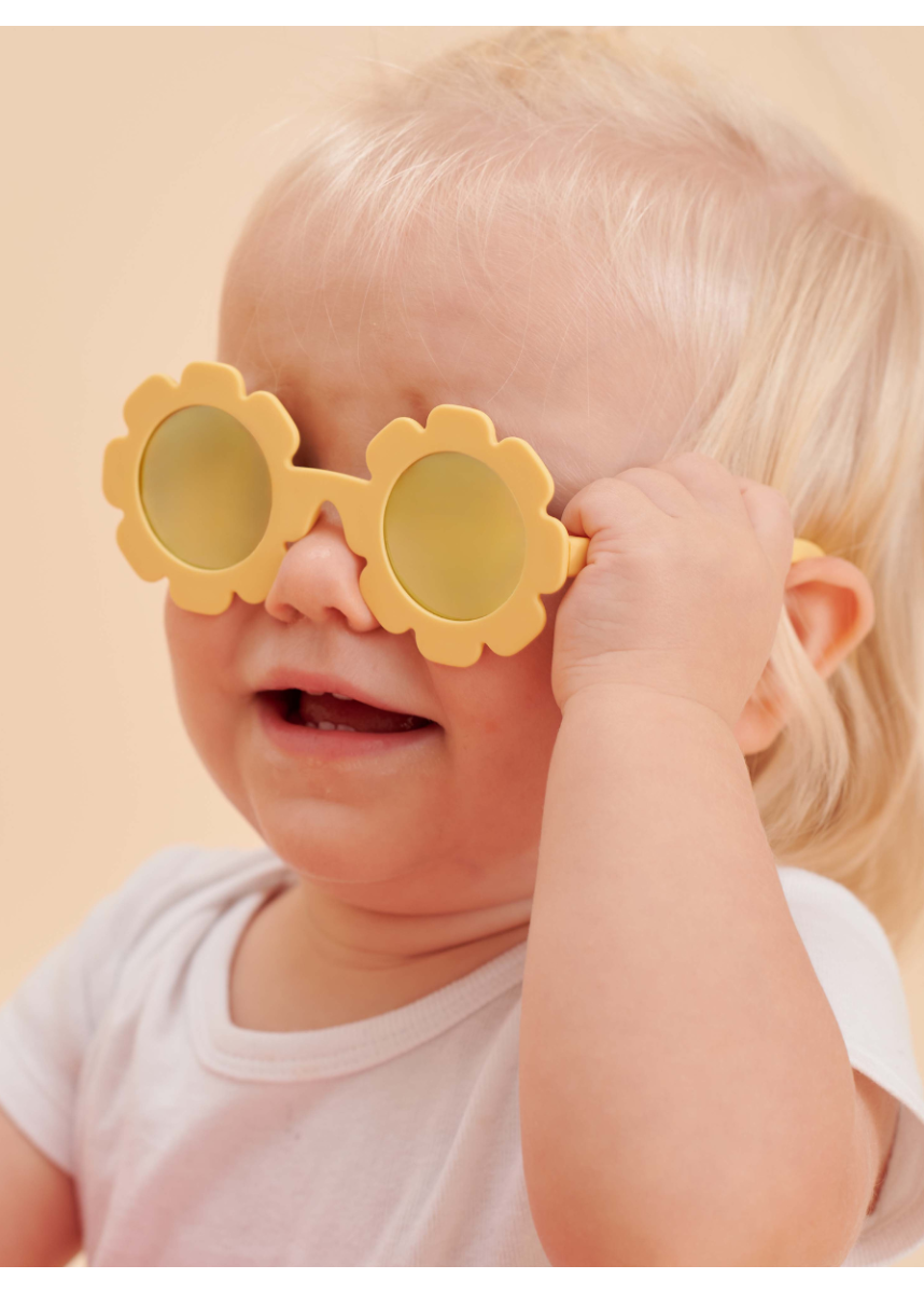 Child wearing yellow flower-shaped sunglasses against a beige background