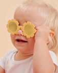 Child wearing yellow flower-shaped sunglasses against a beige background