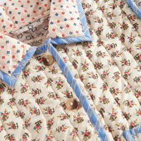 Floral patterned quilt with blue border and decorative pillows on a white background
