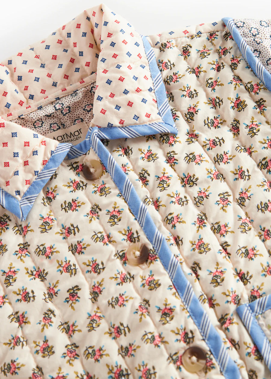 Floral patterned quilt with blue border and decorative pillows on a white background