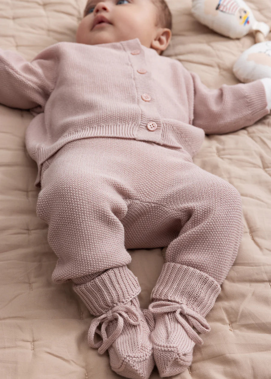 Baby in a pink knitted outfit lying on a beige blanket