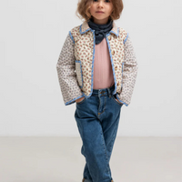Child wearing a patterned jacket, pink shirt, blue jeans, and brown boots on a white background