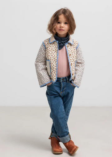 Child wearing a patterned jacket, pink shirt, blue jeans, and brown boots on a white background