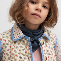 Child wearing a floral jacket and dark scarf against a light background