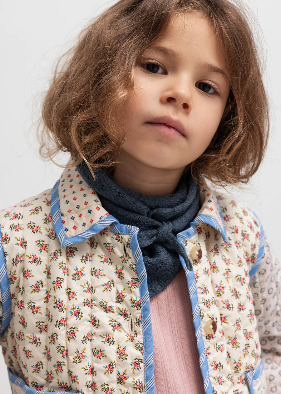 Child wearing a floral jacket and dark scarf against a light background