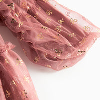 Pink tulle fabric with gold bow patterns on a white background