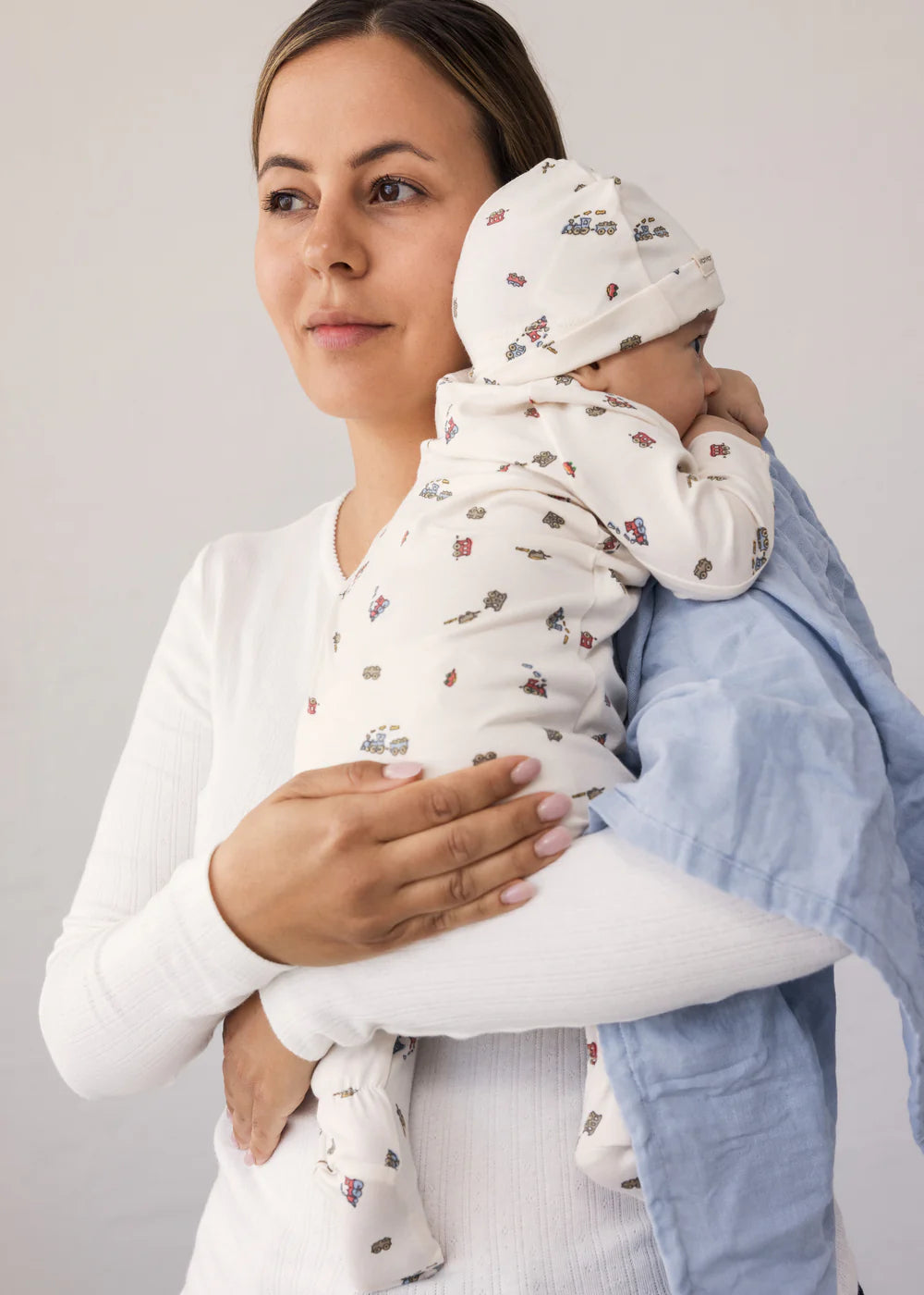 Woman holding a baby wrapped in a swaddle blanket against a plain background