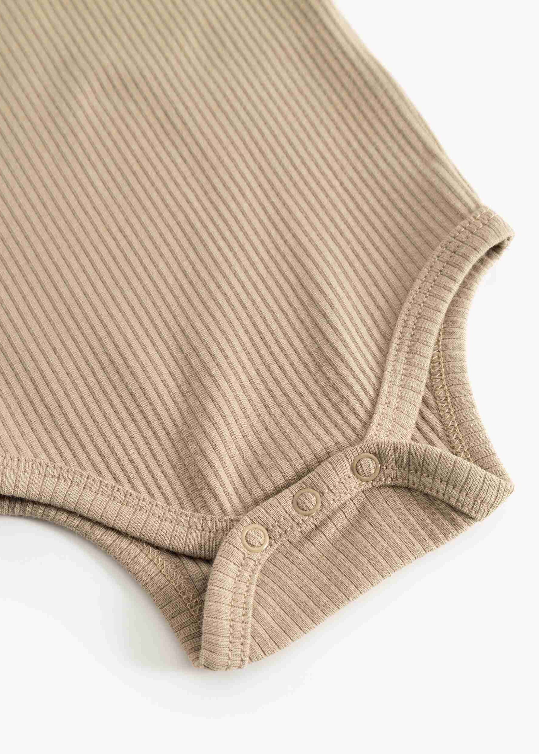 Close-up of a beige ribbed knit baby bodysuit showing the shoulder and snap-button crotch area on a white background.