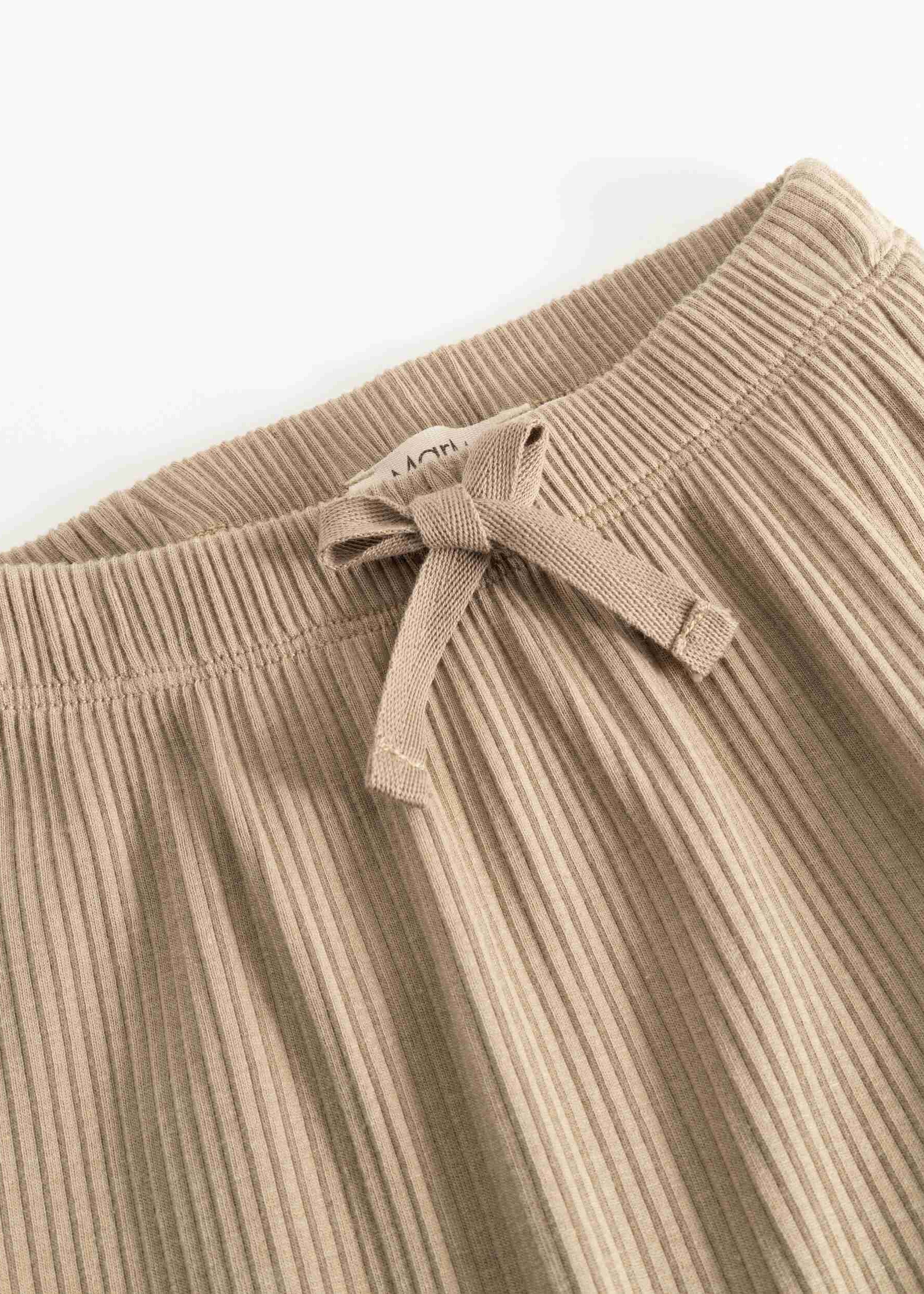 Close-up of beige ribbed knit pants with a matching fabric drawstring bow at the waistband, shown on a plain light background.