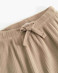 Close-up of beige ribbed knit pants with a matching fabric drawstring bow at the waistband, shown on a plain light background.