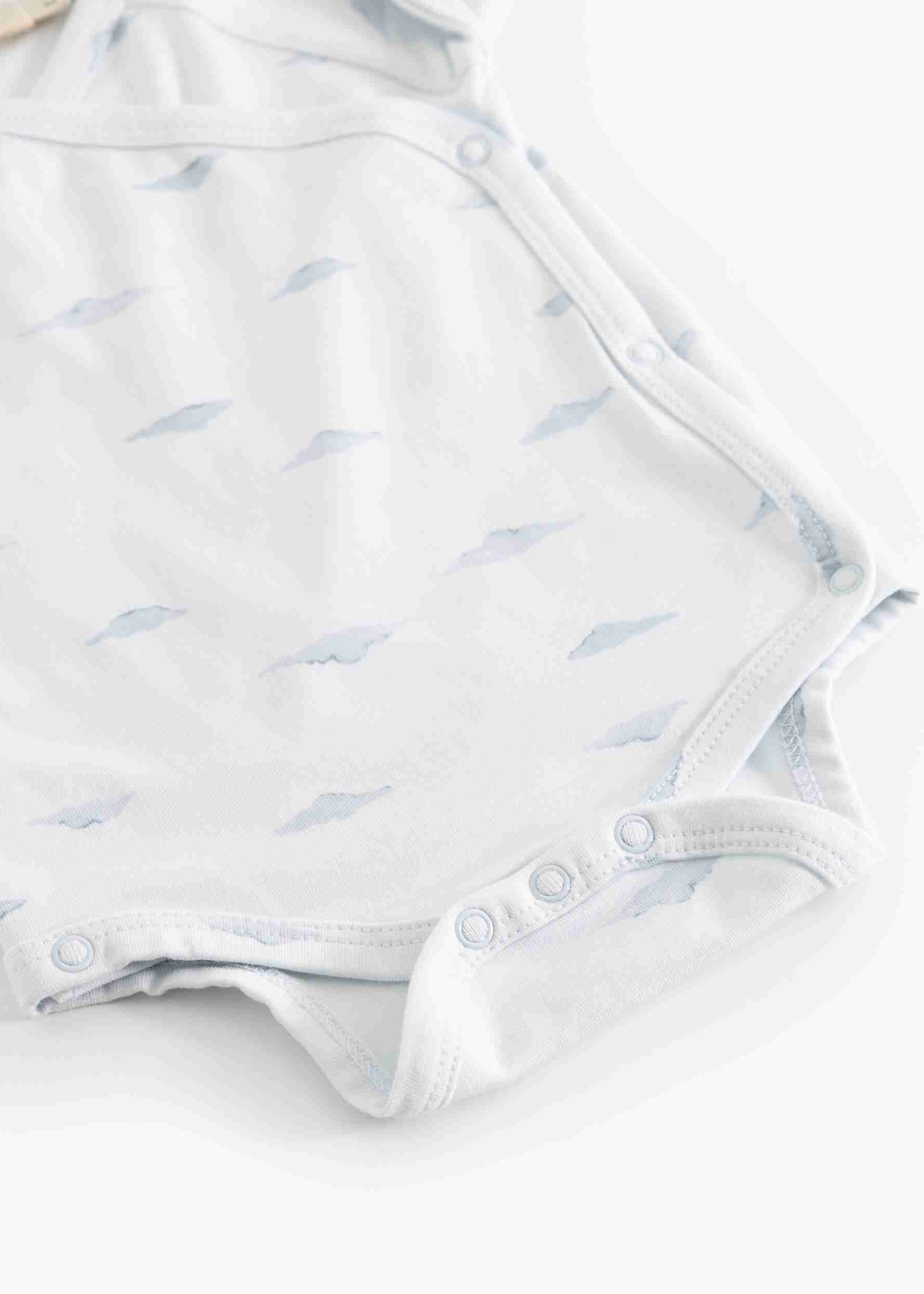 A close-up of a white baby bodysuit featuring a delicate light blue leaf pattern and snap closures along the shoulder and crotch.