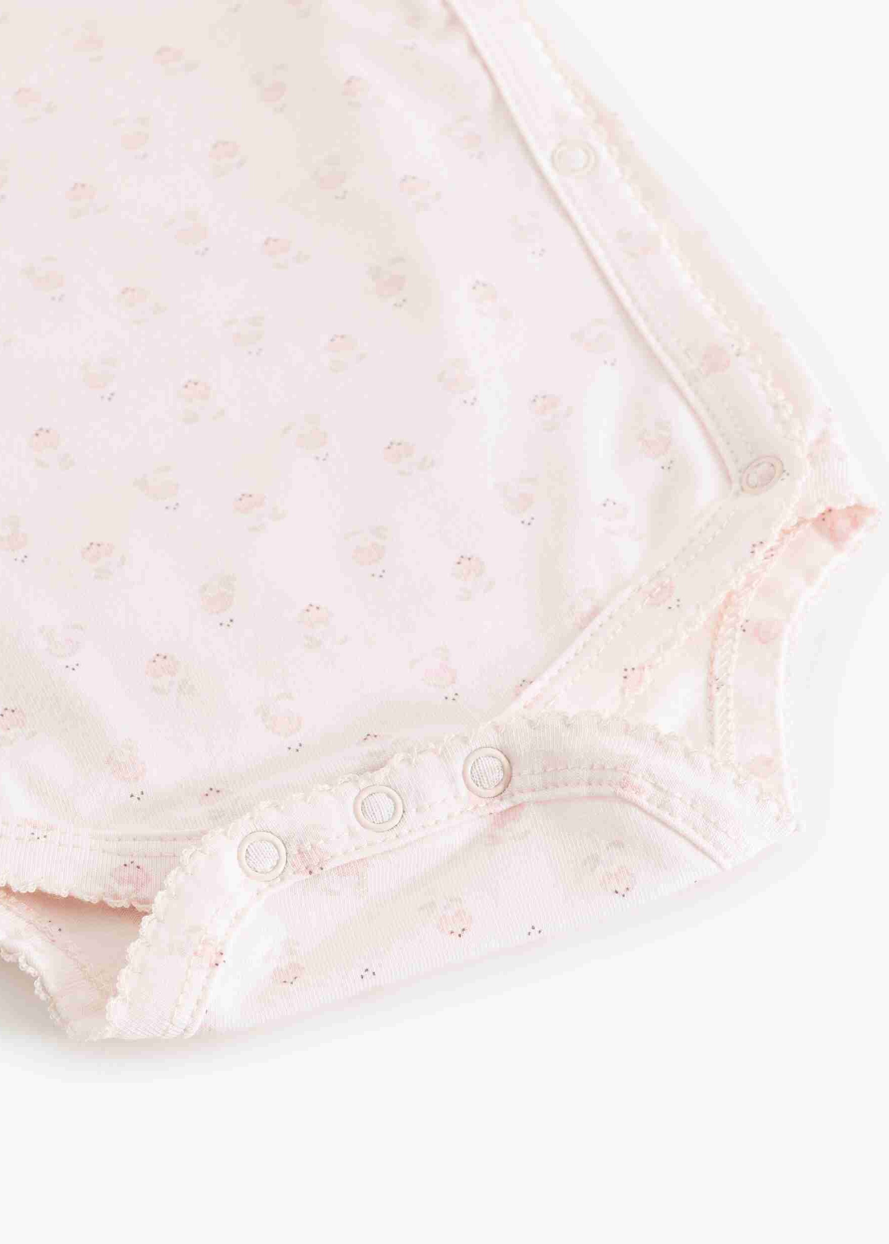 Close-up of a baby bodysuit in pale pink with a tiny floral print and snap closures along the shoulder.