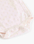Close-up of a baby bodysuit in pale pink with a tiny floral print and snap closures along the shoulder.